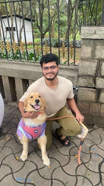 A young man kneeling with a Golden Retriever puppy in a harness