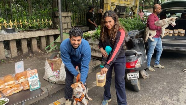 A couple greeting a small indie dog at the ChewCheer sampling stall
