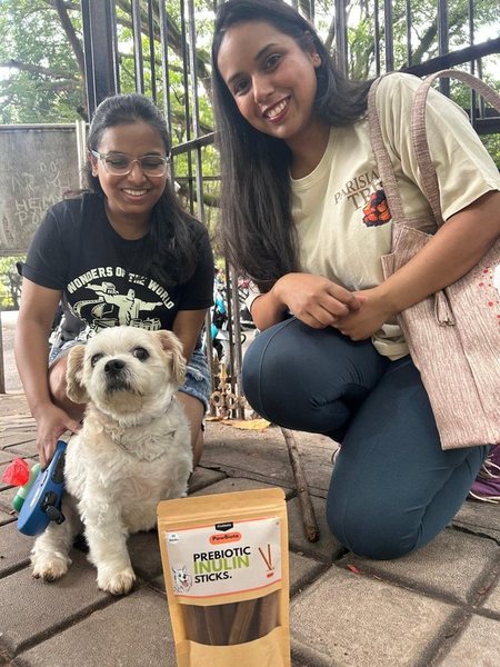 Two friends crouching with a small white Shih Tzu and a pack of prebiotic sticks